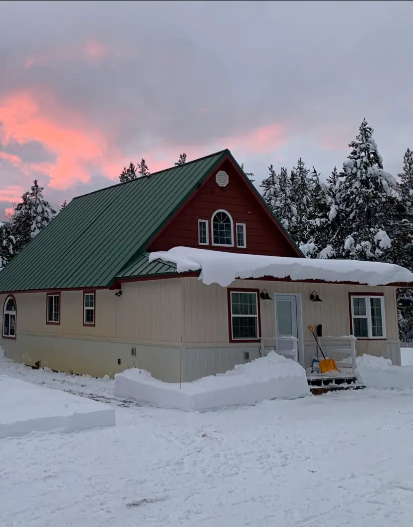 A house with snow on the roof and trees in the background.