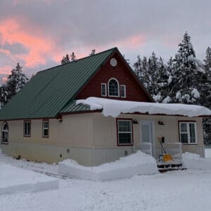 A house with snow on the roof and trees in the background.