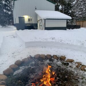 A fire pit in the snow with a white building behind it.