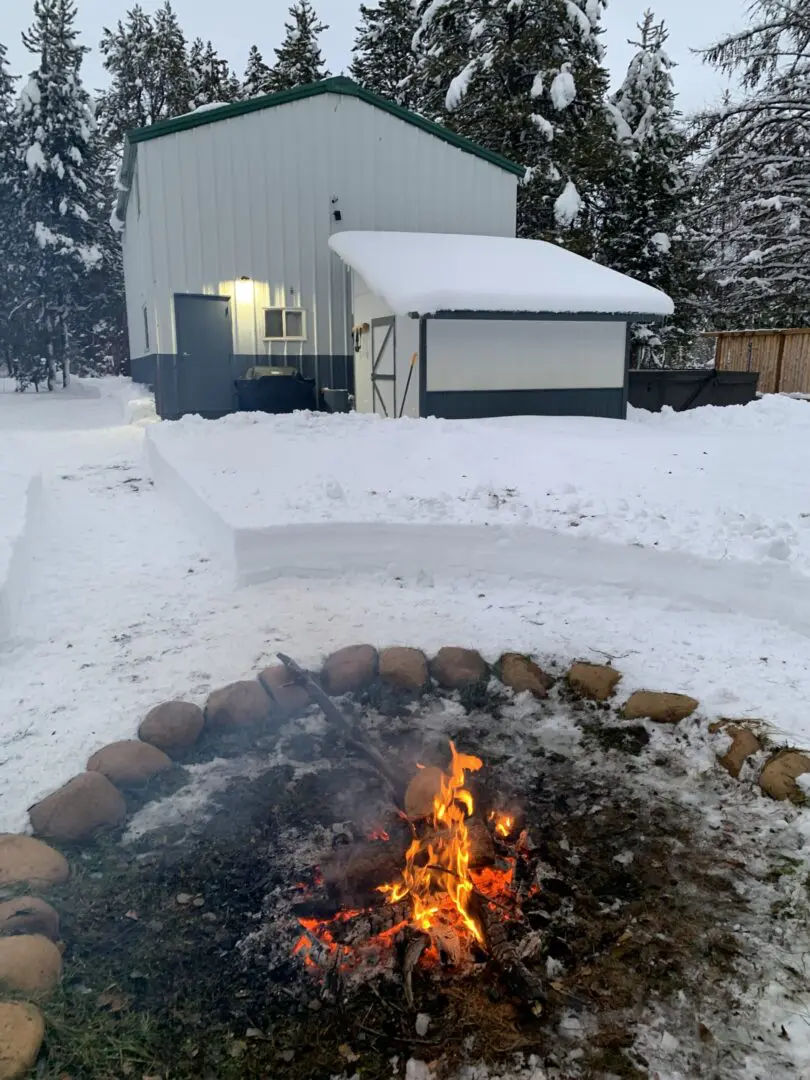 A fire pit in the snow with a white building behind it.