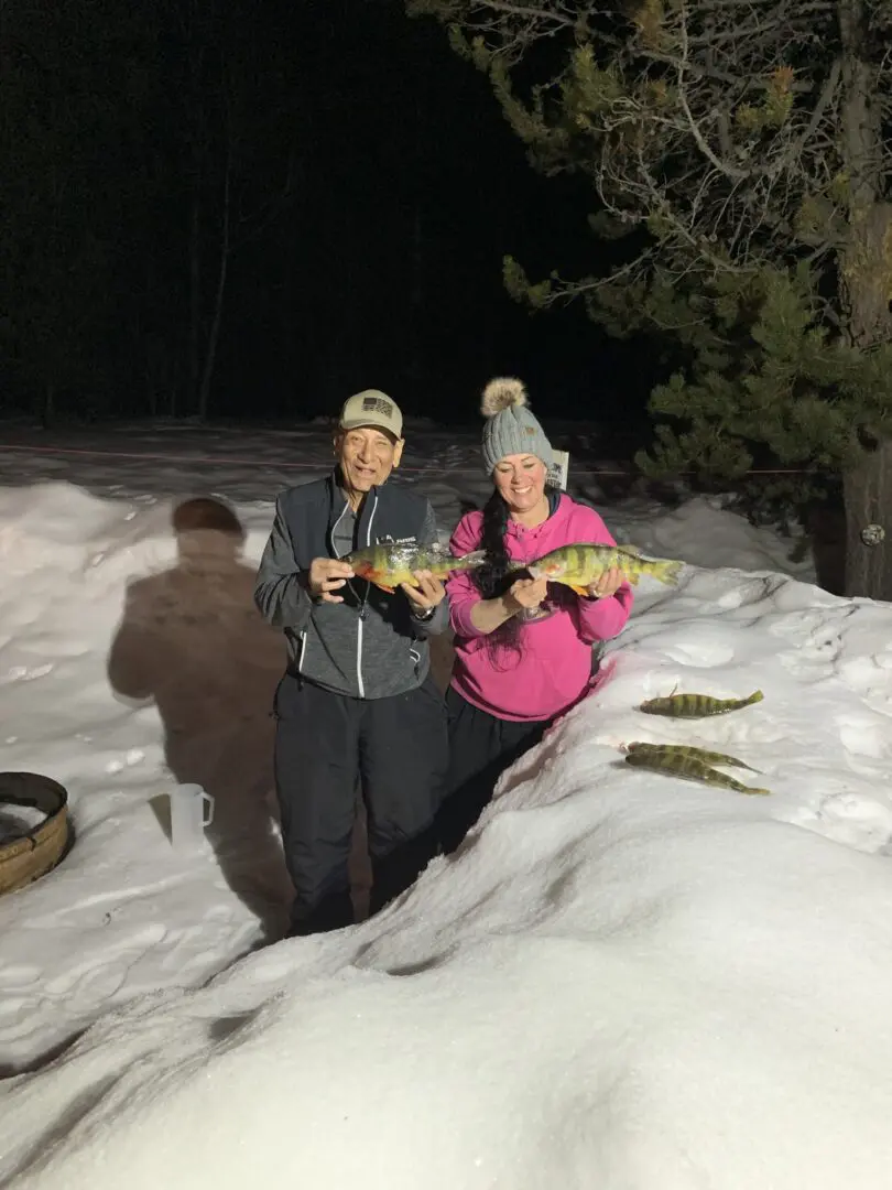 Two people standing in the snow holding fish.